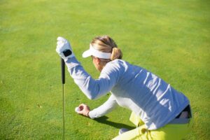 a woman lining up her ball to the cup on the green.